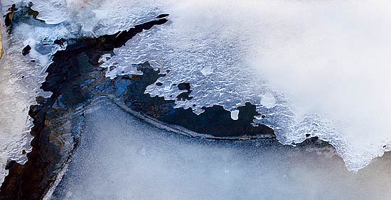 photo: lacy ice hovers over melting ice in the black water.