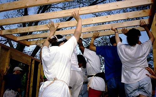 photo: Habitat for Humanity volunteers with their arms in the air carrying a wall frame.