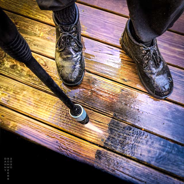 Photo of a pressure washer’s wand blasting a wooden deck with water by Danny N. Schweers